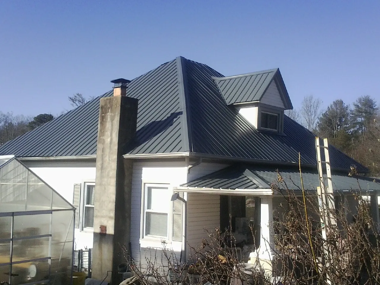 Dark blue standing seam metal roof on a white farmhouse with dormer — Slate & Tile Roof Repair by Roofing Brothers in Carney