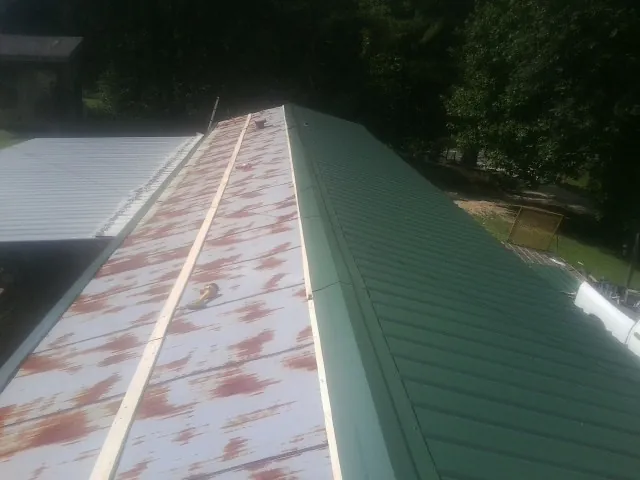 Old rusted panels beside newly installed green metal roofing — Wind Damage Roof Repair by Roofing Brothers in Carney