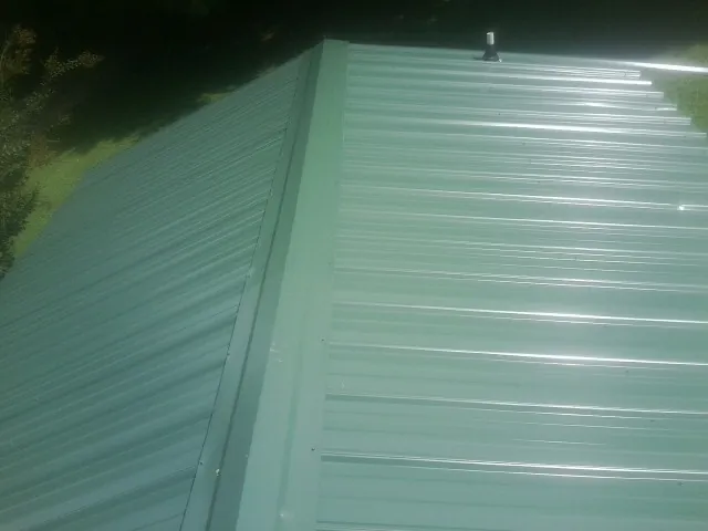 New green metal panels meeting at the ridge of a roof — Flat Roof Repair work by our crew in Carney
