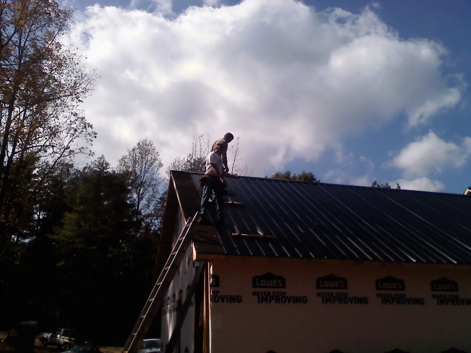 Roofer fastening dark metal panels high against a cloudy sky, from a Roof Inspection job in Carney