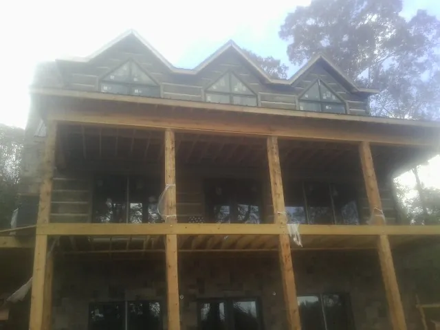 Dormers and porch framing on a large log home under construction — Roof Coating work by our crew in Carney