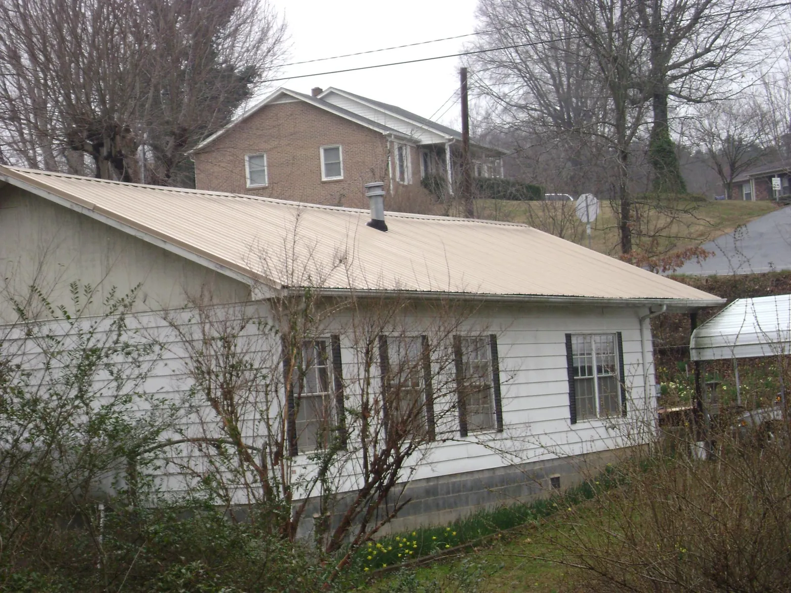 Tan metal roof on a white sided house set into a hillside — Commercial Roofing by Roofing Brothers in Carney