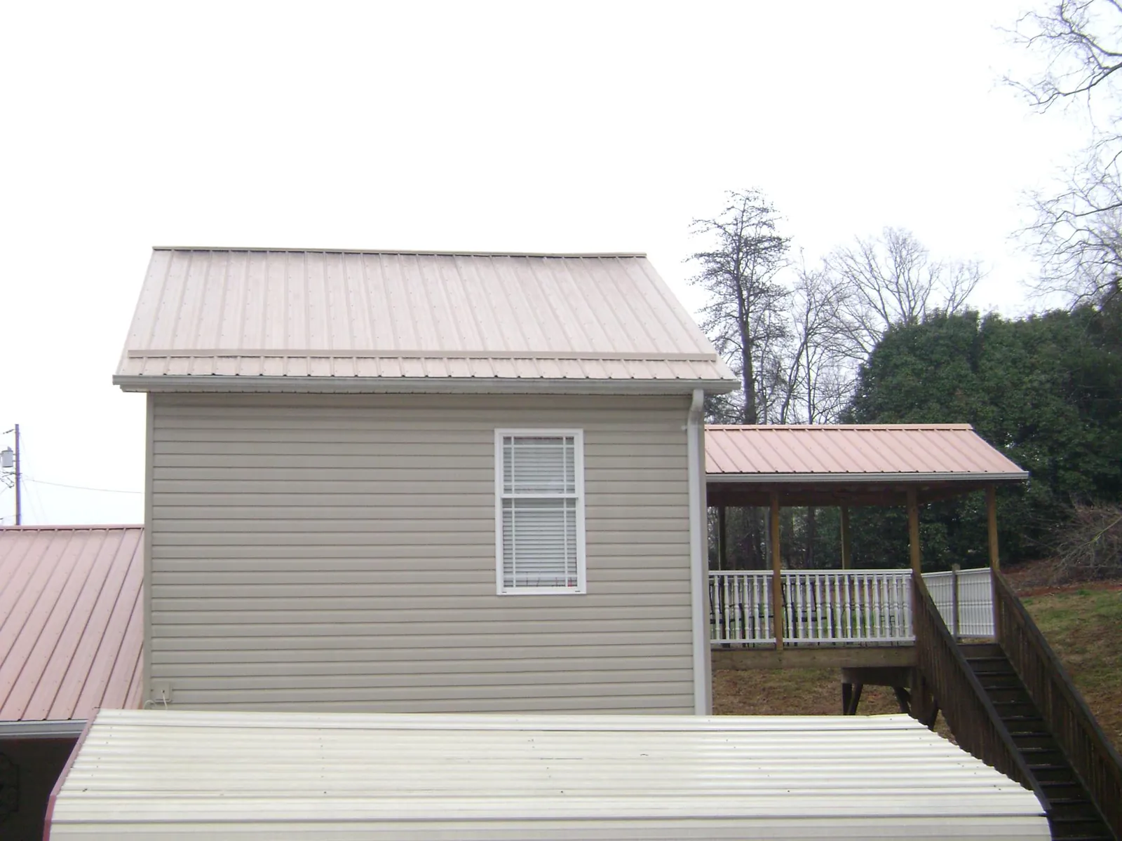 Tan metal roofs on a two story addition and attached porch, from a Roof Replacement job in Carney